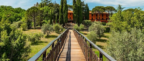 A wooden bridge leading to a building with a red facade, surrounded by greenery.
