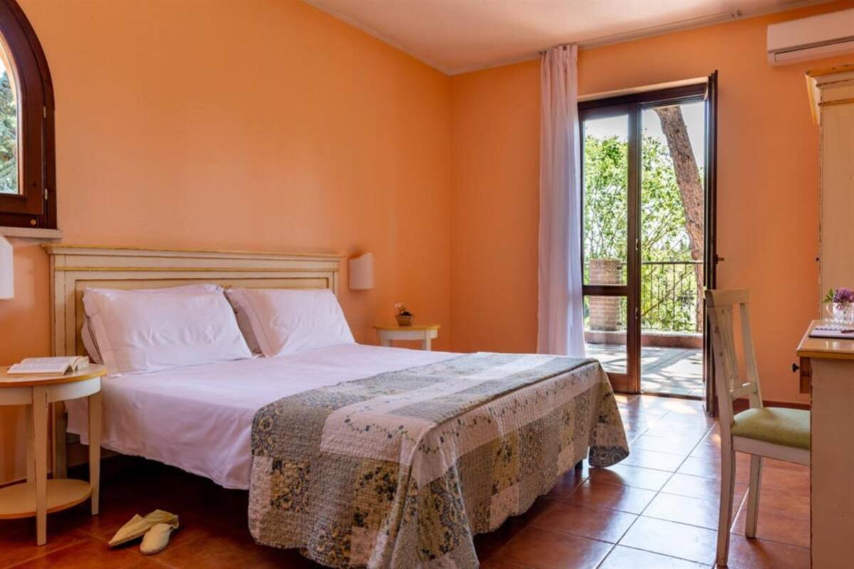 A bedroom with a bed, a nightstand, a chair, and a view of the outdoors through a glass door.