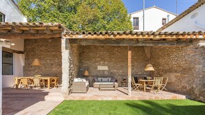 A stone-walled patio with outdoor furniture, a grassy lawn, and a white building in the background. - Finca Can Romeu: Alojamiento Rural Entre Viñedos (Guardiola De Font-Rubi)