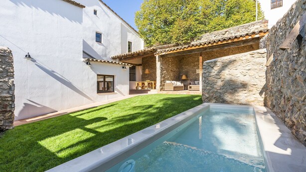A swimming pool with a stone wall and a grassy area. - Finca Can Romeu: Alojamiento Rural Entre Viñedos (Guardiola De Font-Rubi)
