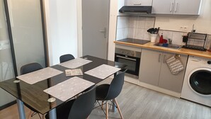 A modern kitchen with a dining table, chairs, an oven, a washing machine, and a sink. - F1 Duplex Entièrement Rénové (Lamalou-les-Bains)
