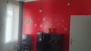 A room with a red wall, a black cabinet, a white door, and a window with sheer curtains. - F1 Duplex Entièrement Rénové (Lamalou-les-Bains)