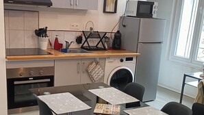A modern kitchen with stainless steel appliances, a dining table with patterned placemats, and a view of the outside through a large window. - F1 Duplex Entièrement Rénové (Lamalou-les-Bains)