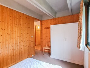 A bedroom with wooden walls, a white wardrobe, and a chair.