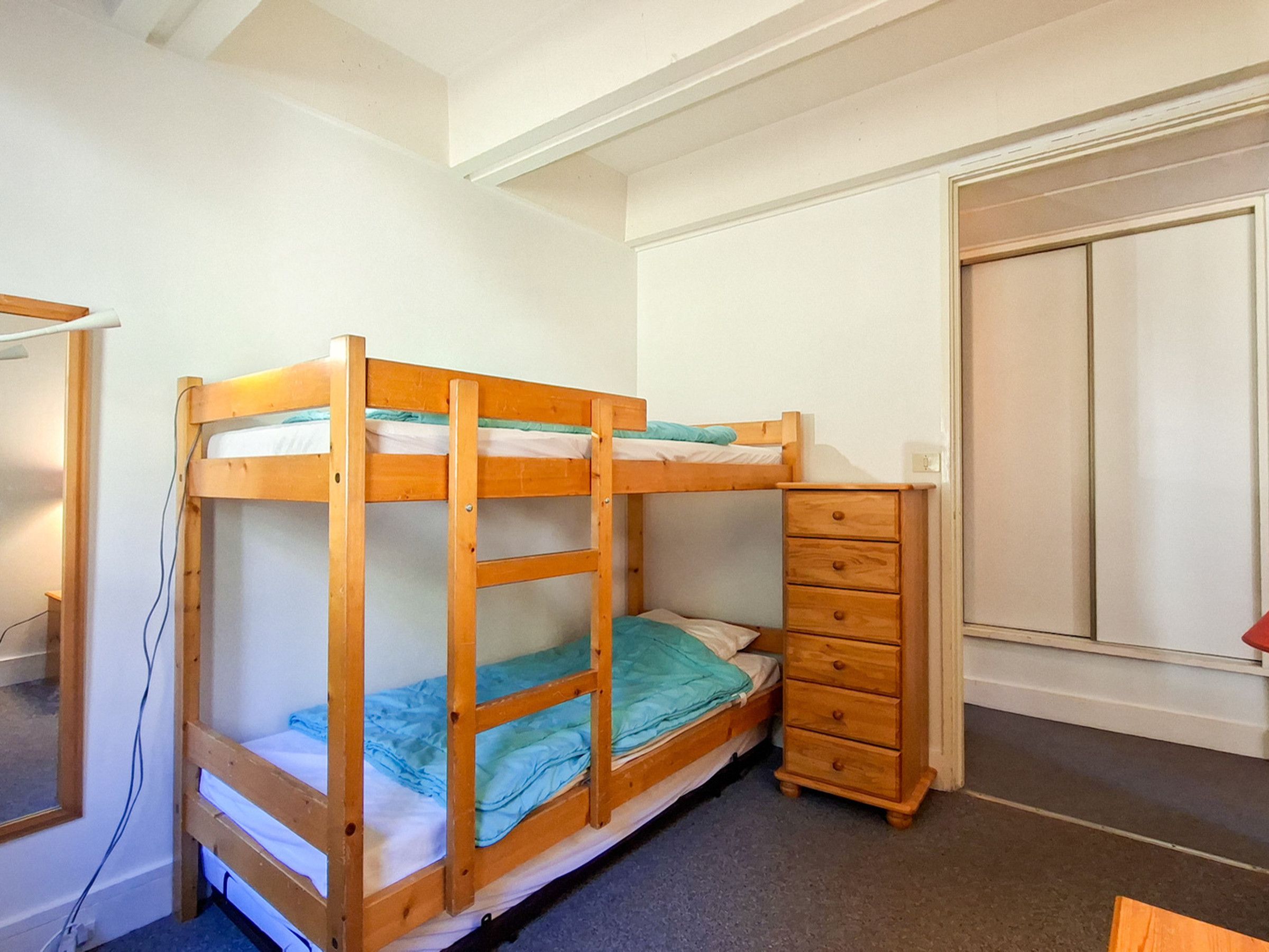 Una cama litera con un aparador de madera a un lado, un armario y una ventana.