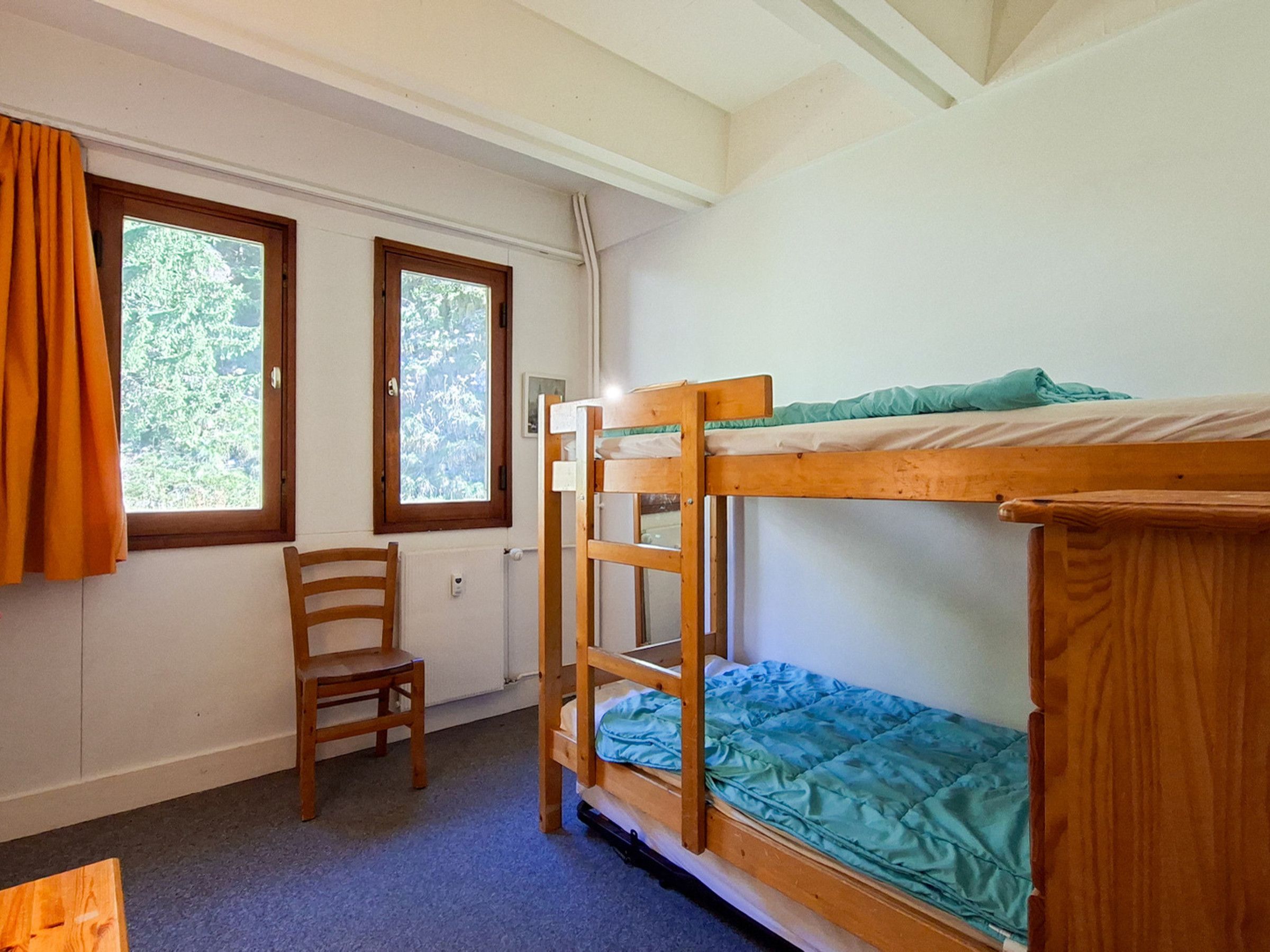 A bunk bed room with a chair and two windows.