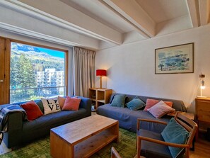 A cozy living room with two sofas, a wooden coffee table, and a chair. There is a window with a view of a mountain and buildings.