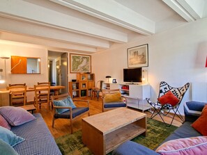 Ein Wohnzimmer mit einer Couch, einem Couchtisch, einem Fernseher und einem Essbereich mit Stühlen und einem Tisch.