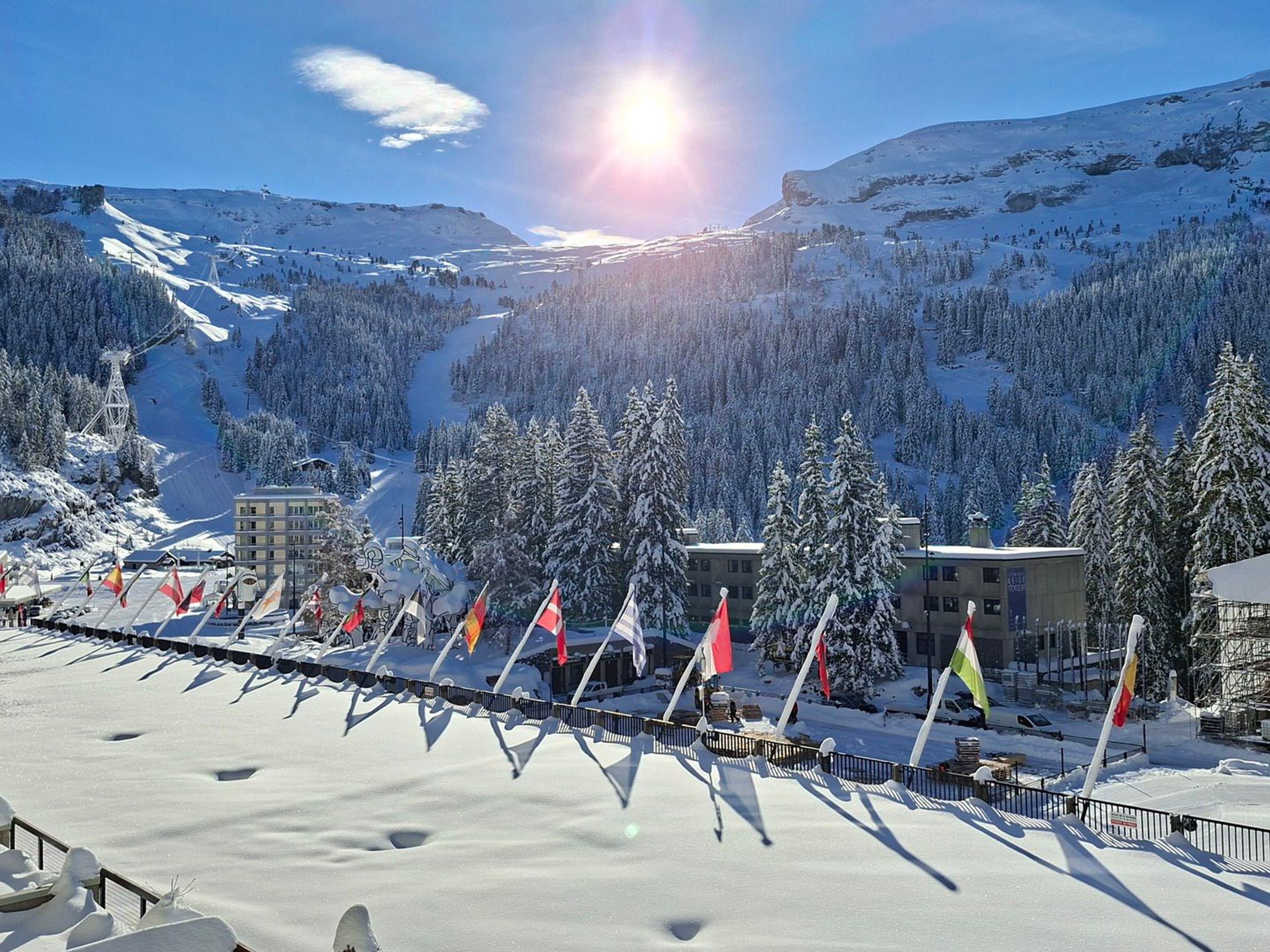 A snow-covered mountain landscape with a ski resort, buildings, and flags.