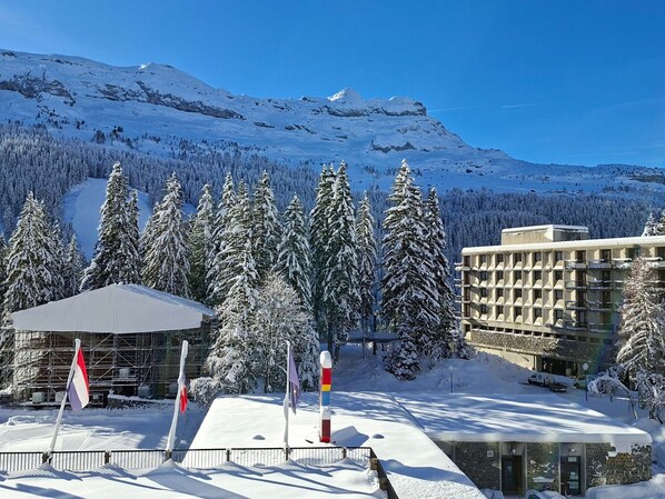 A hotel with a snow-covered mountain backdrop, a parking area, and a building with a modern design.