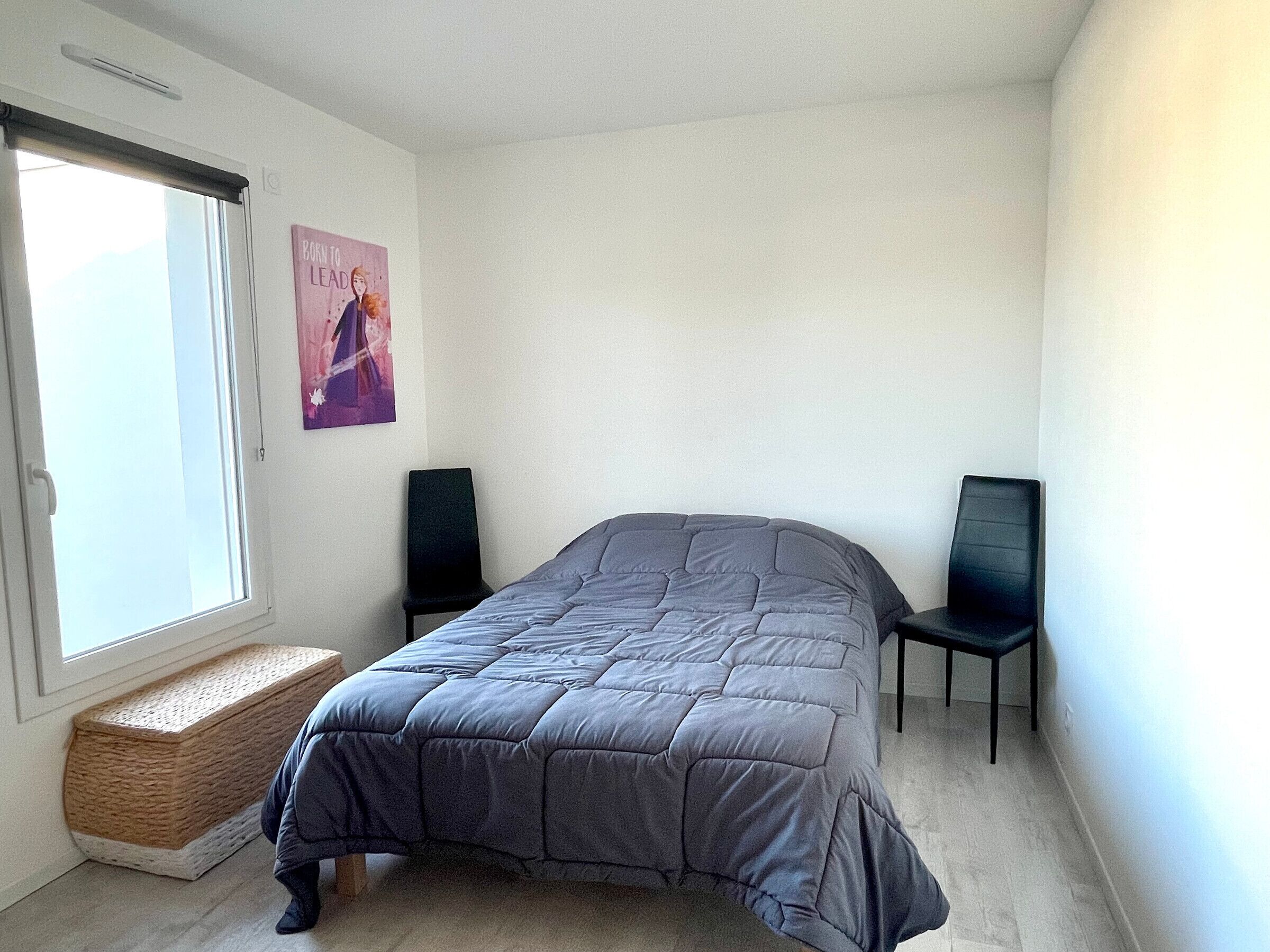 Une chambre à coucher avec un lit, une fenêtre, une chaise et une affiche accrochée au mur.