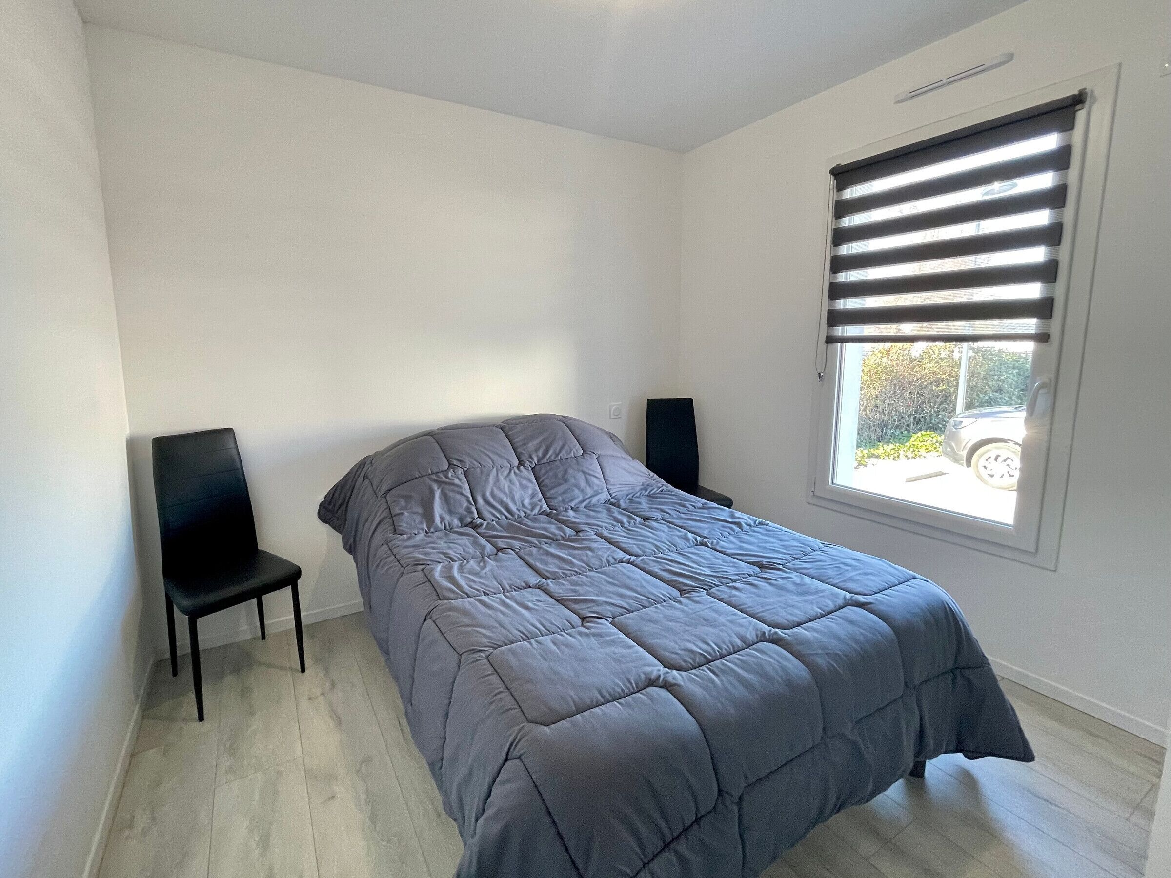 A bedroom with a bed, a chair, a window with blinds, and a speaker.