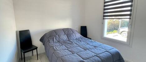 A bedroom with a bed, a chair, a window with blinds, and a speaker.