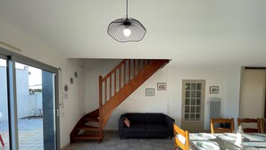 Un comedor con una mesa de madera dispuesta para cuatro personas, un sofá de color oscuro y una escalera que sube a otro nivel.