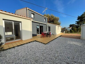 Ein zweistöckiges Haus mit einer Terrasse, die einen Tisch und Stühle bietet.