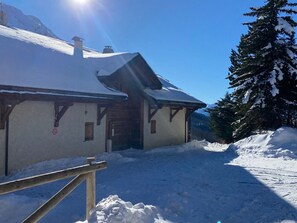 A snow-covered lodge with a wooden facade, a chimney, and a wooden fence in the foreground.