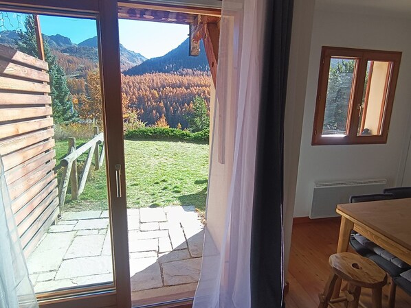 A room with a wooden deck, a view of a forested mountain, and a small table with a bench.