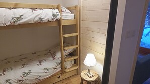 Ein kleiner, kompakter Raum mit einem Etagenbett, einer Holzleiter, einem kleinen Hocker und einem an der Wand befestigten Regal.