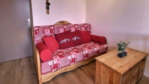 A cozy room with a wooden floor, a red patterned sofa, a small wooden table, and a wall-mounted rifle. - Cozy 2-room in Vallandry, 4 guests, near slopes and shops (Peisey-Vallandry)