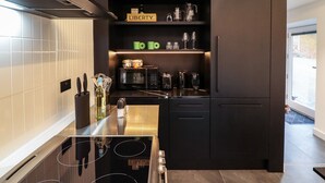 A modern kitchen with a black refrigerator, a built-in oven, and a microwave. There are shelves above the oven with glassware and a sign that reads "LIBERTY." - The Pump House Forge (Doncaster)