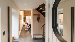 A modern hallway with a brick wall, a staircase, and a dining area with red chairs. - The Pump House Forge (Doncaster)