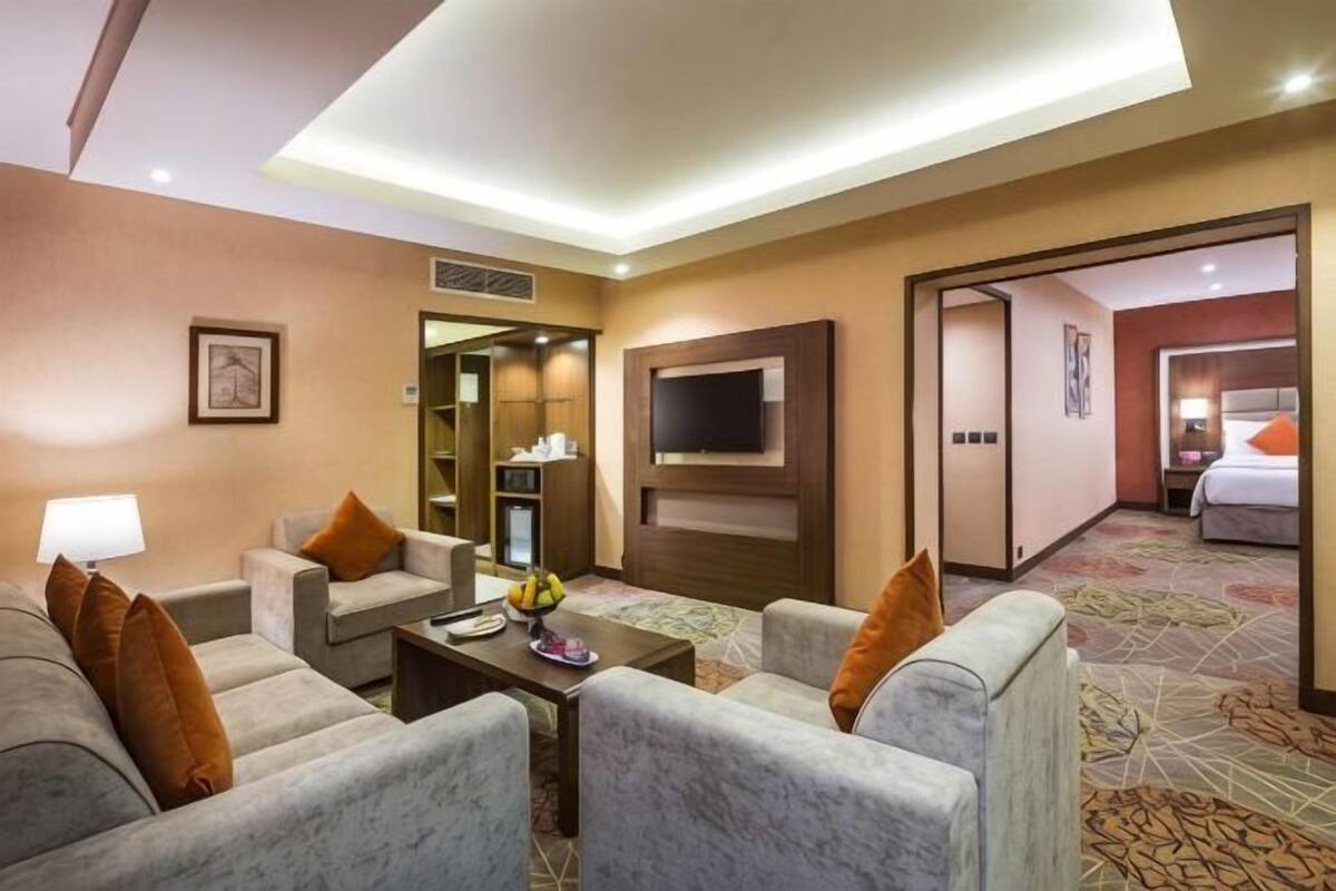 A hotel room with a seating area, a flat-screen TV, a bed, and a bathroom visible through an open door.