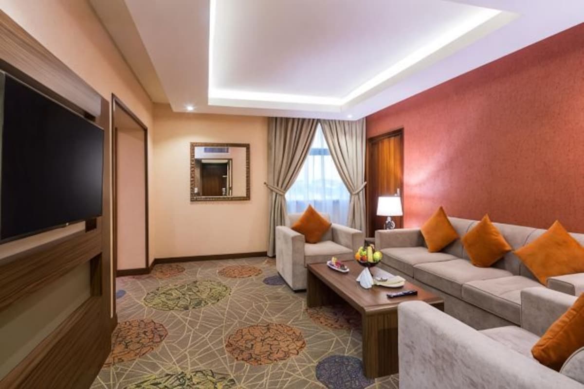 Habitación de hotel con una televisión, dos sofás, una mesa de centro y una alfombra estampada.