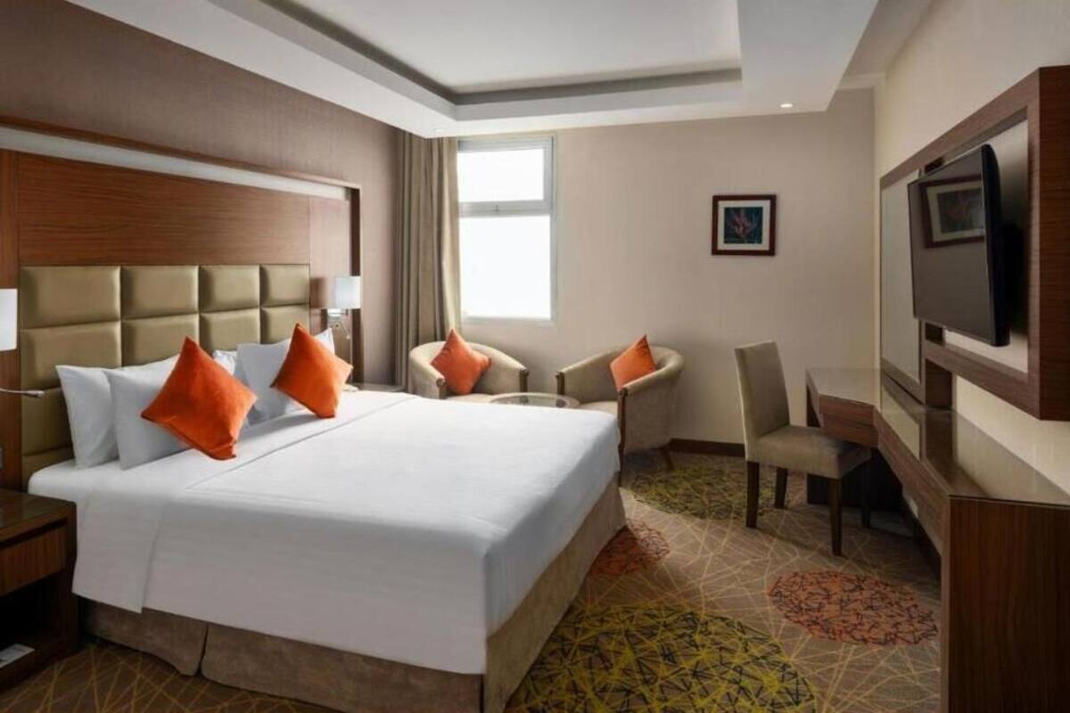 A hotel room with a large bed, two armchairs, a desk, a TV, and a window.
