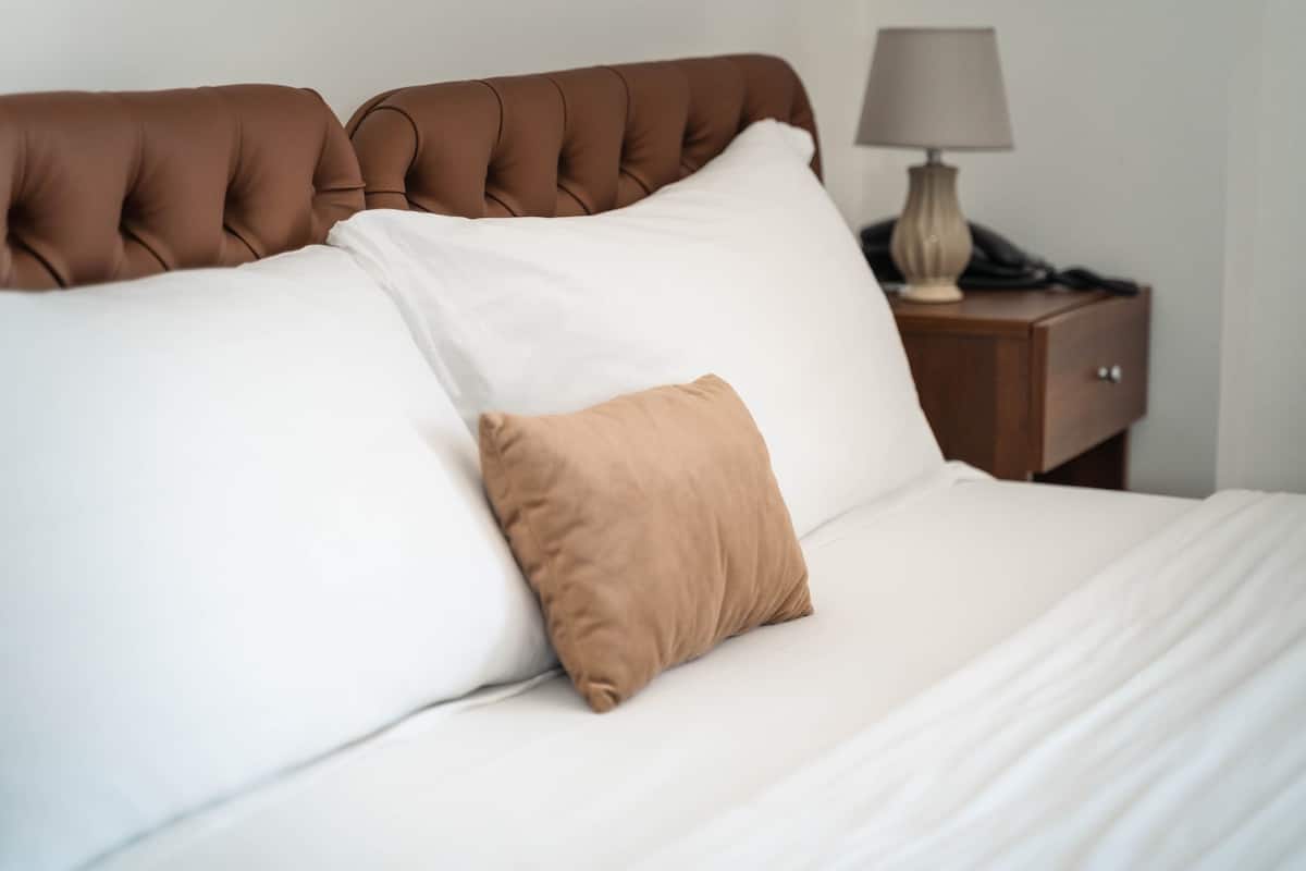 A neatly made bed with a brown headboard, white pillows, and a brown accent pillow.