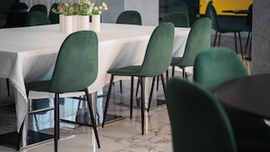 Un comedor con una mesa blanca, sillas verdes y un florero con flores.