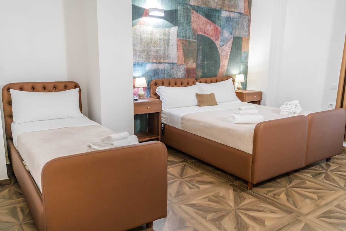 A hotel room with two beds, a nightstand with a lamp, and a colorful abstract painting on the wall.