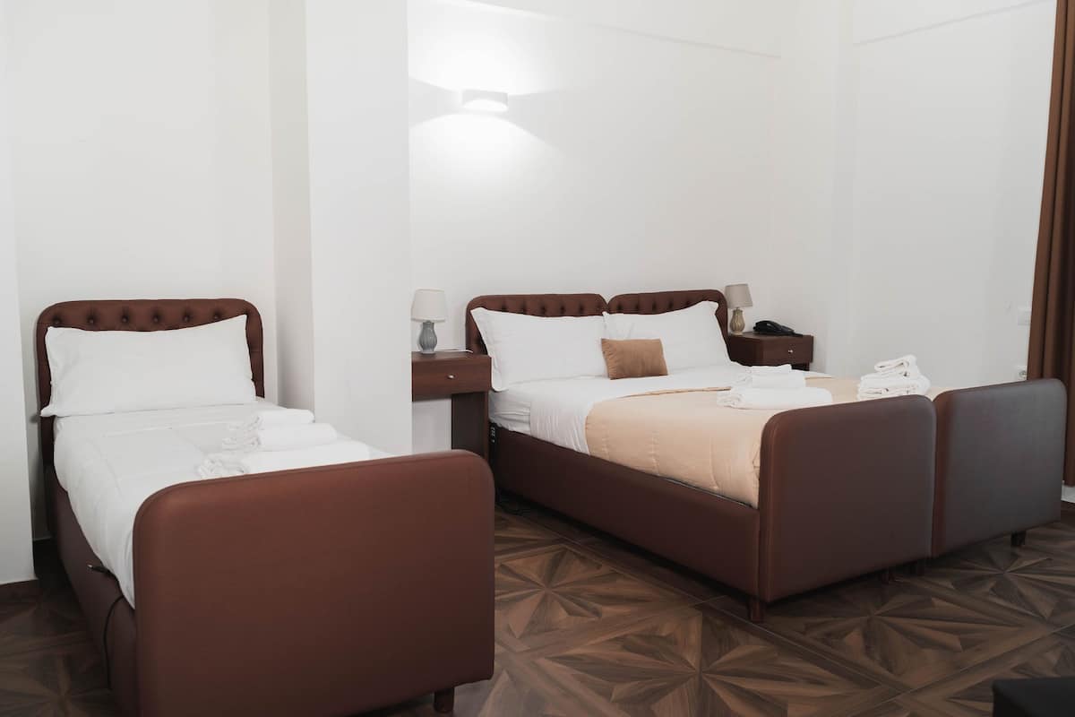 A hotel room with two single beds, a nightstand with a lamp, and a patterned floor.