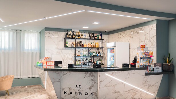 Una recepción con mostrador de mármol, diversas botellas de licor y el logotipo de 'KAIROS'.