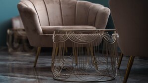 Una habitación moderna con un sillón rosa mullido, una mesa redonda de metal con un diseño original de alambre y un suelo oscuro.