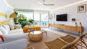 Een moderne woonkamer met een bank, rieten stoelen, een ronde salontafel en een televisie aan de muur.