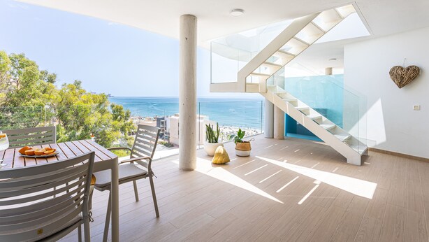 Een modern interieur met een trap, een eethoek met een tafel en stoelen, en uitzicht op zee.