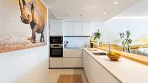 Een moderne keuken met witte kastjes, een ingebouwde oven en een groot eiland met een fruitschaal.