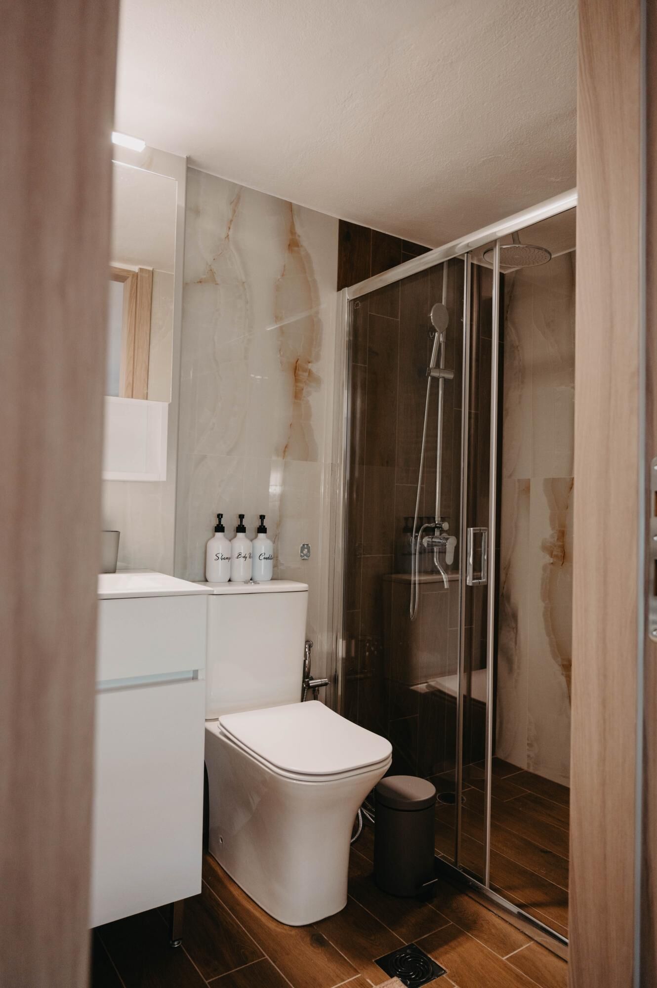 A modern bathroom with a glass-enclosed shower, a toilet, and a vanity with toiletries.