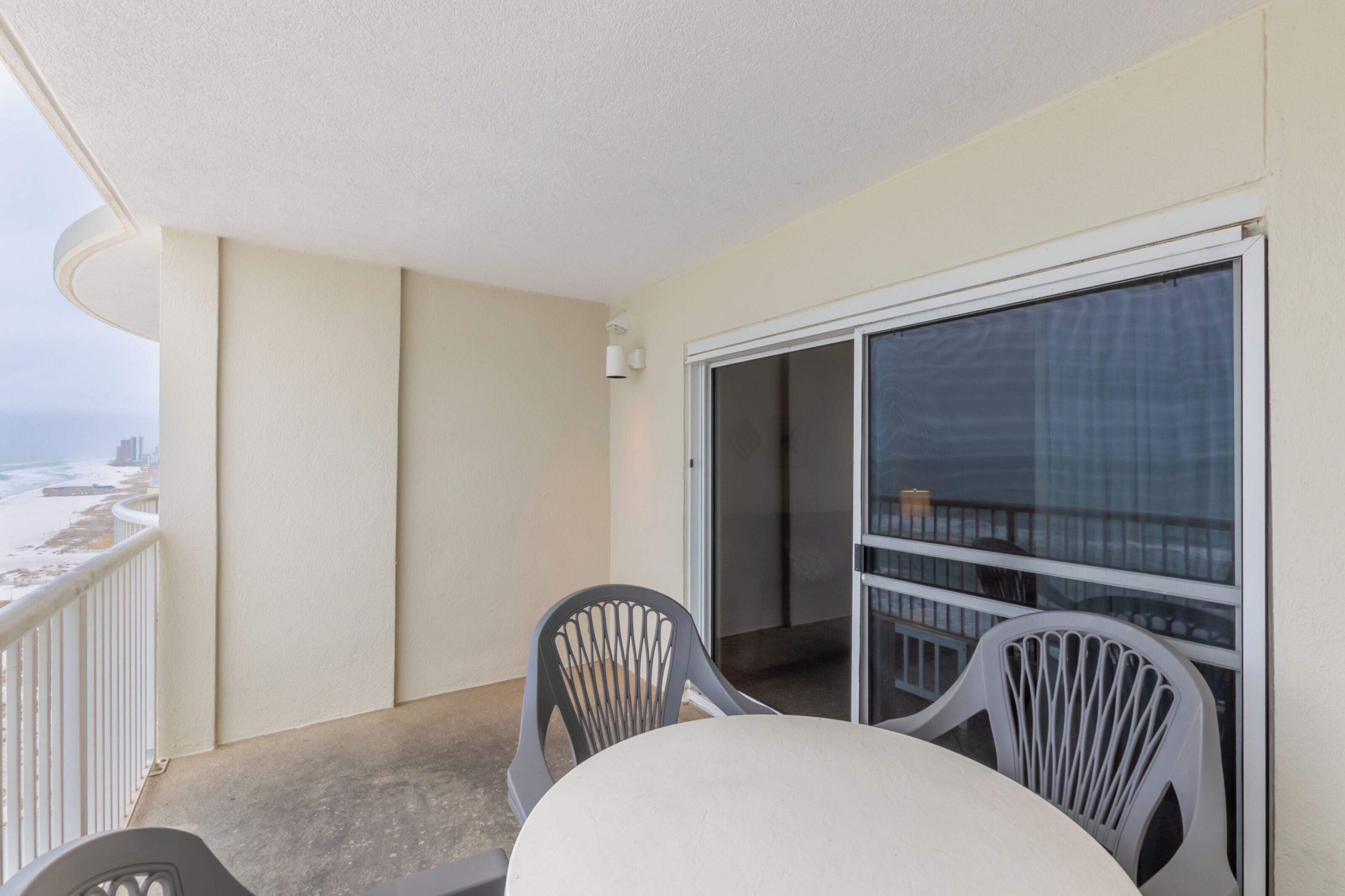 Un balcon avec une table et deux chaises, une porte-fenêtre coulissante et une vue sur la plage et le paysage urbain.