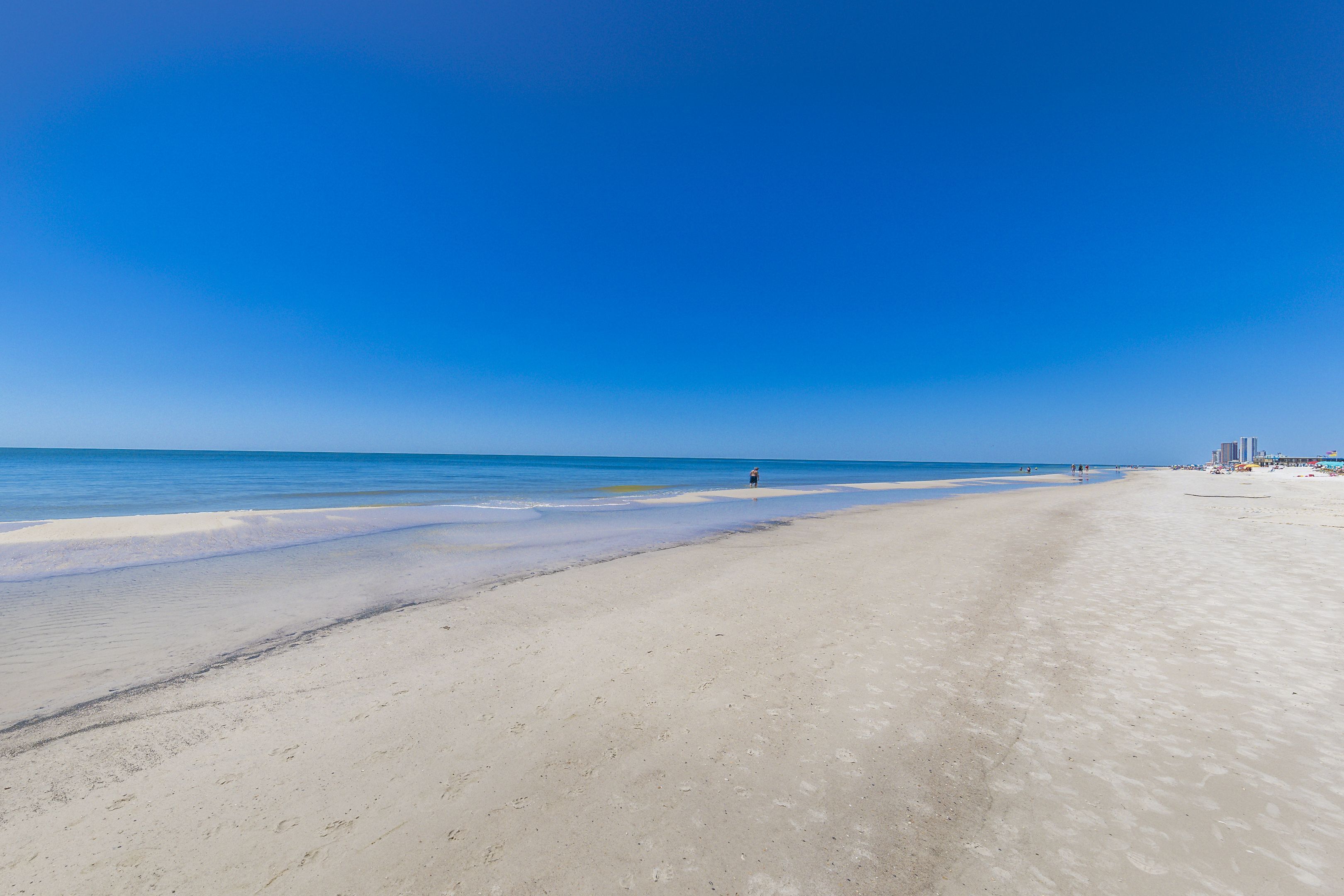 Ampia spiaggia sabbiosa con acque cristalline e alcune persone in lontananza.