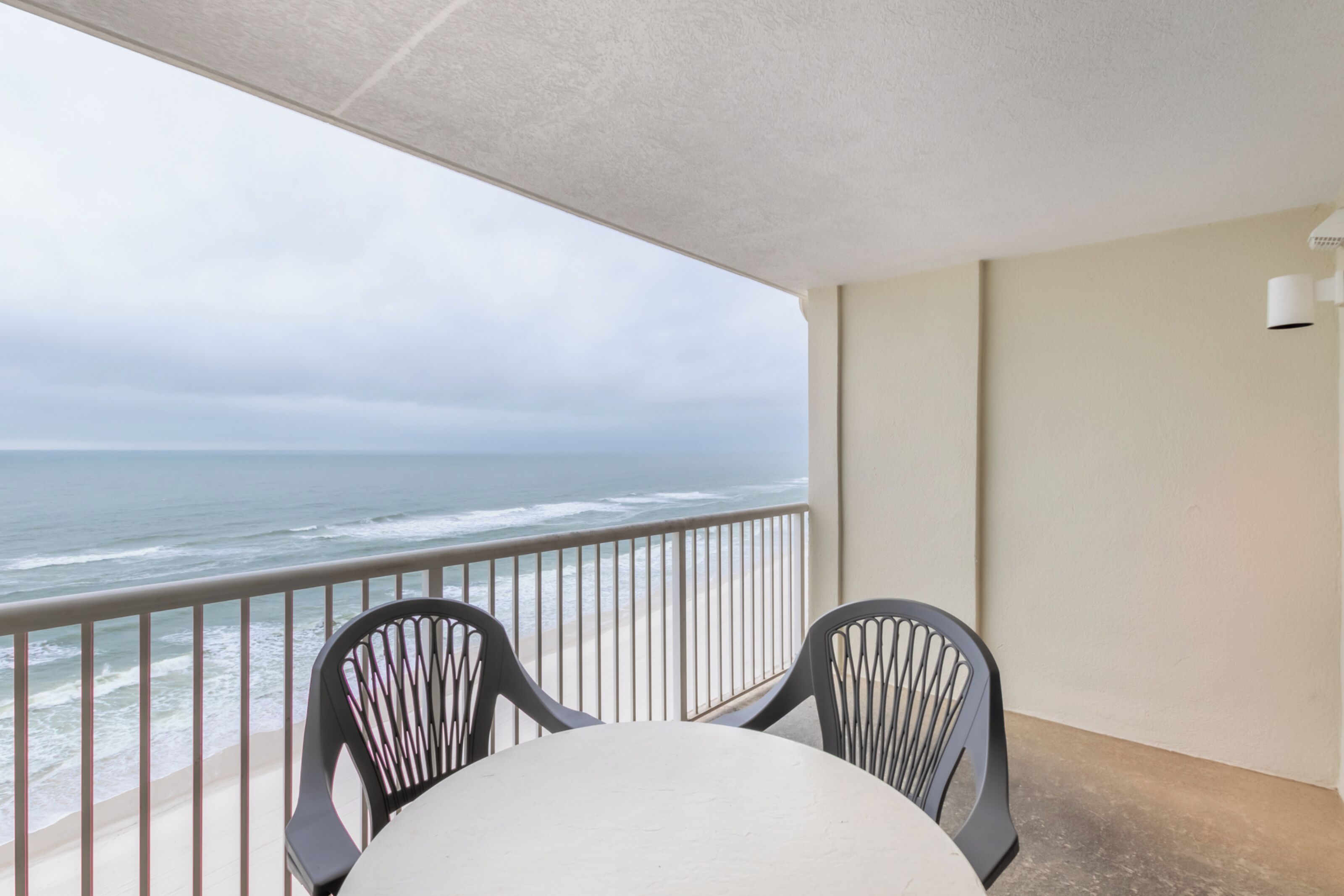 Un balcon avec vue sur l’océan, deux chaises et une table.