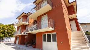 Un immeuble résidentiel à plusieurs étages, doté de balcons, d’un garage et d’un escalier menant à l’entrée.