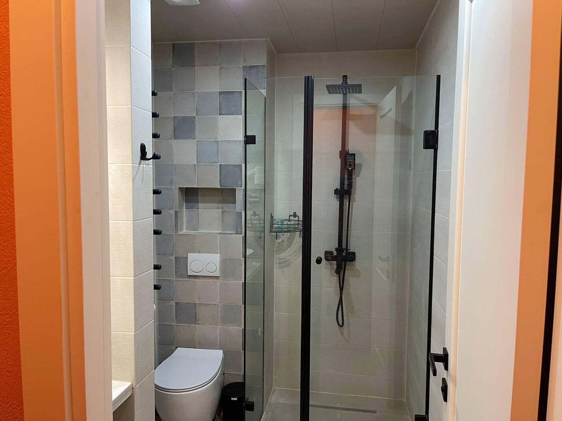 Een compacte badkamer met een douchecabine, toilet en een klein schapje.