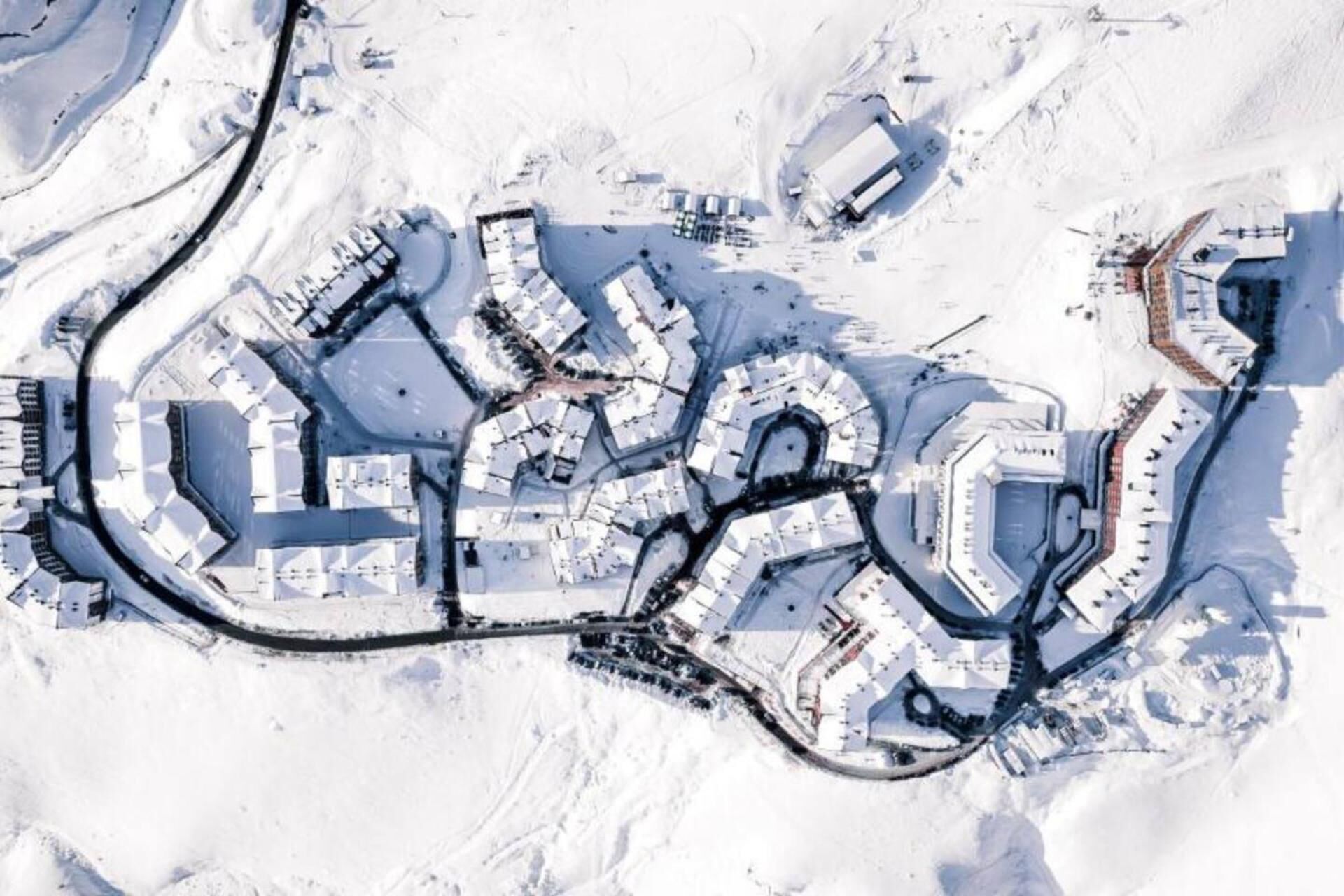 Vue aérienne d’une zone enneigée comprenant plusieurs bâtiments, des routes et une grande structure circulaire.