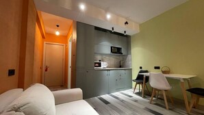 A compact room with a sofa, a dining table with chairs, a kitchenette, and a door leading to another room.