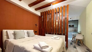 A bedroom with a bed, pillows, a wooden partition, a radiator, a small table, and a chair.