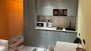 A compact kitchen with grey cabinets, a microwave, a kettle, and a built-in oven.