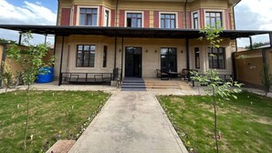 A two-story house with a covered front porch, a central entrance, and a small front yard with a pathway leading to the door. - Hotel Karaman (Tashkent)