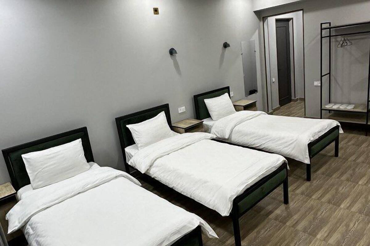 A hotel room with four single beds, a wooden floor, and a mirror on the wall.