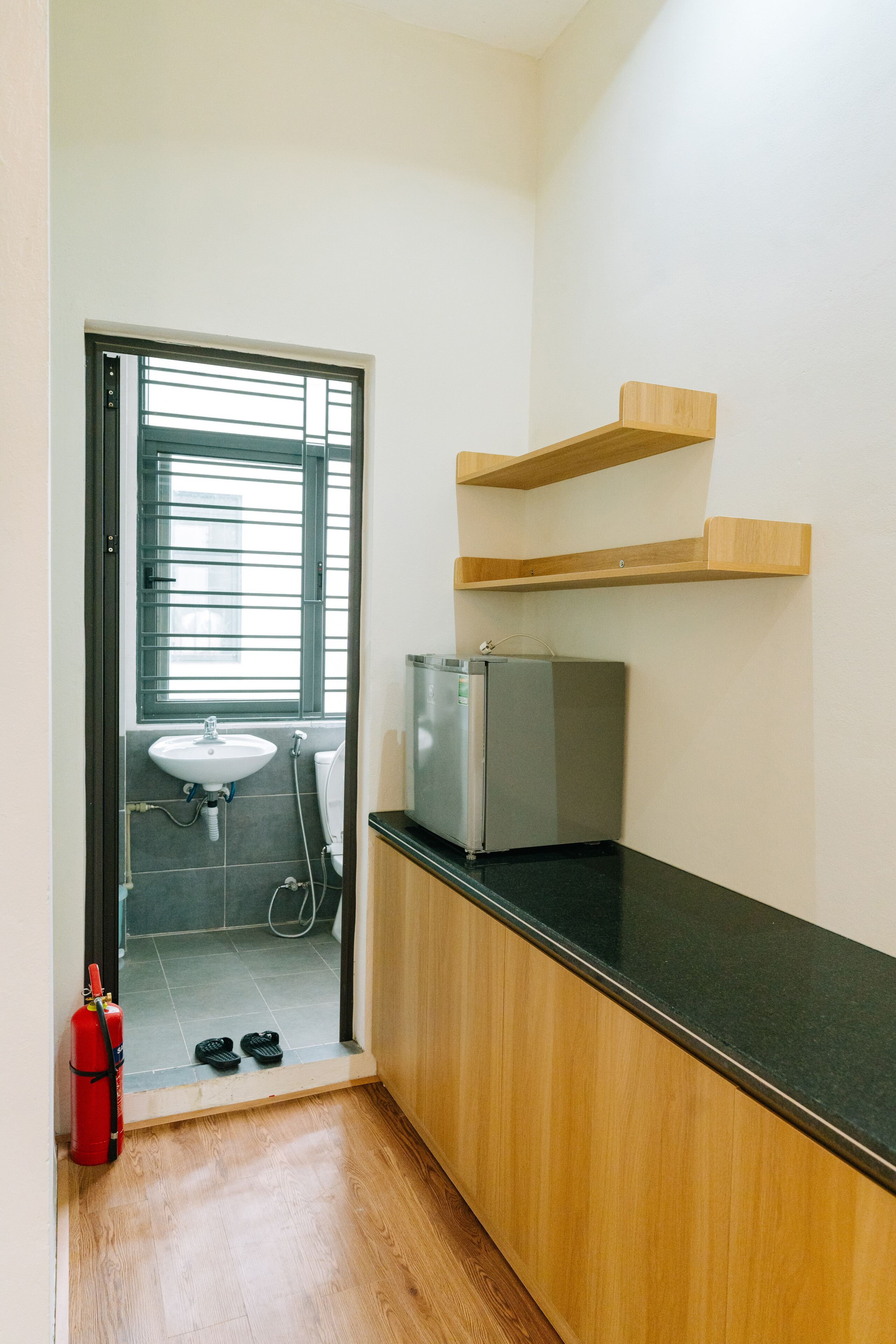 A small kitchenette with a refrigerator, a sink, and wooden shelves.